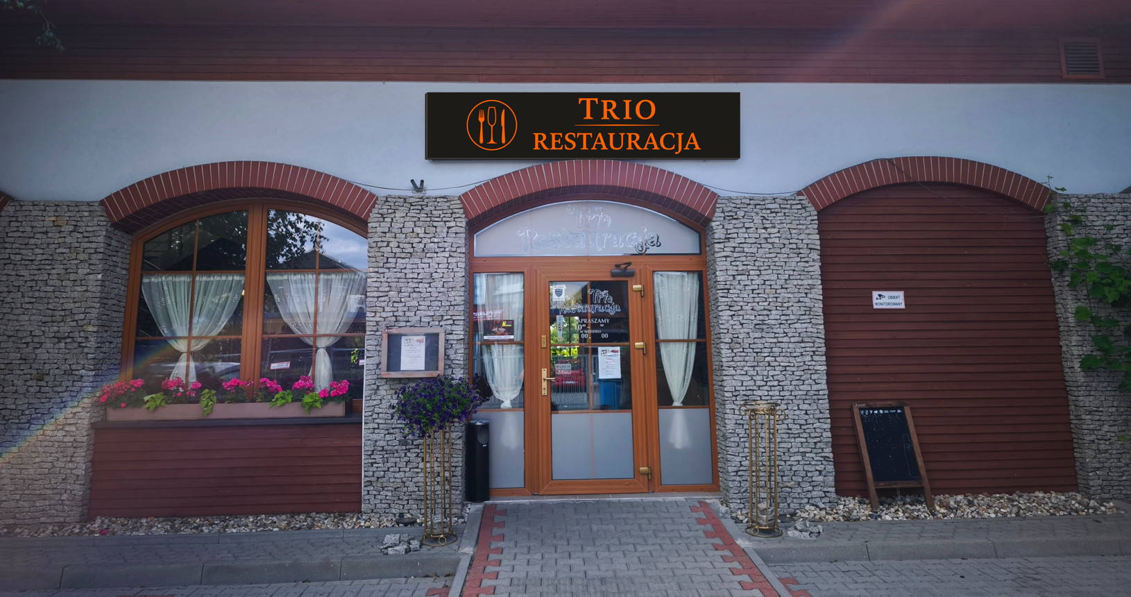 Widok na front Restauracji TRIO w Opolu - przytulna, kamienna fasada z łukowymi oknami i podświetlonym szyldem.